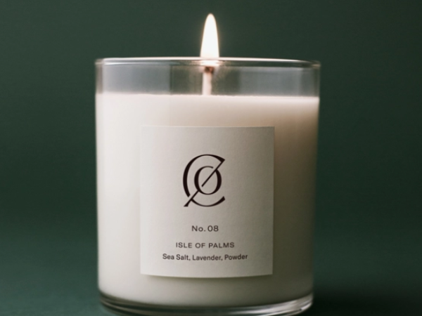 A lit candle in a glass container labeled "Isle of Palms" with scents of sea salt, lavender, and powder against a dark green background.