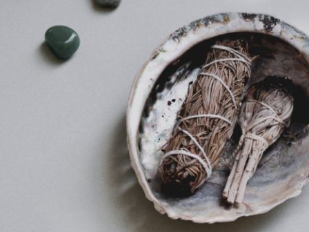 A shell holds smudge sticks, surrounded by green stones, likely used for spiritual or cleansing practices.