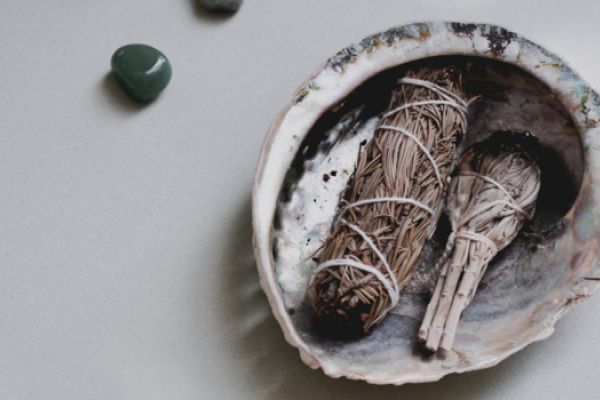 A shell holds smudge sticks, surrounded by green stones, likely used for spiritual or cleansing practices.