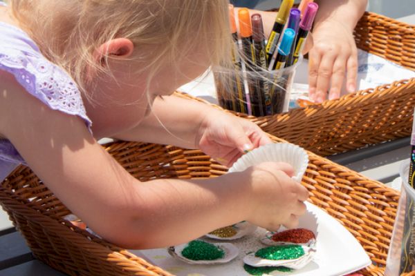 A child is decorating paper with glitter, using markers and paints, with art supplies in baskets.
