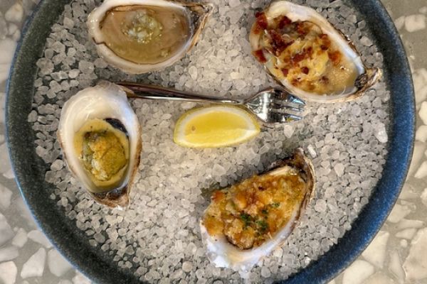 A plate with four oysters on ice, garnished with lemon wedges and a fork in the center.