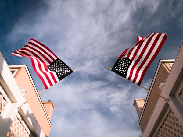 Two American flags waving between two buildings against a partly cloudy sky.