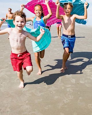 Children running on the beach holding colorful bodyboards, smiling and enjoying the sunny day.