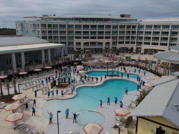 A large group of people in blue shirts stand around a pool at a resort, forming a heart shape with their arrangement.