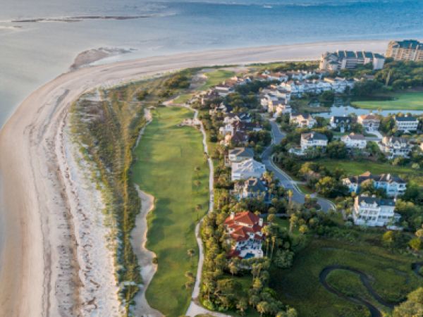Aerial view of a coastal area with a beach, ocean, residential homes, greenery, and a golf course.