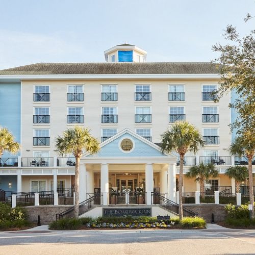 The image shows a large, elegant hotel building with palm trees in front and a clear sky.