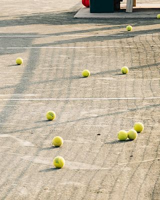 Tennis balls scattered on a court with lines and a net in the foreground.
