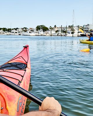 People kayaking on a calm body of water with a view of boats and houses in the background.