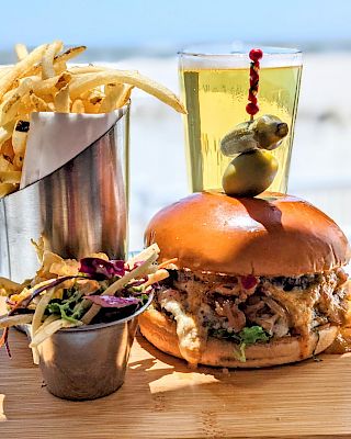 Burger with pulled pork, fries in a cup, a salad, and a drink garnished with olives on a wooden board.