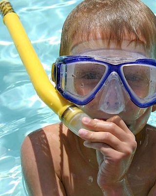 A child in a pool wearing a blue snorkel mask and a yellow snorkel, smiling and enjoying the water.