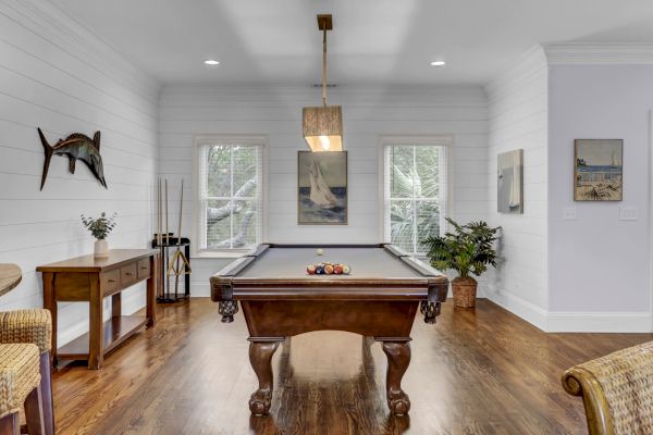 A room with a pool table, wooden floor, wall art, plants, and a side table with a vase, creating a cozy ambiance.