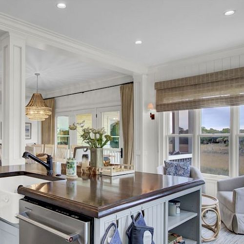 A bright, modern kitchen with an island, bar stools, pendant lights, and large windows providing a scenic view of the outdoors.