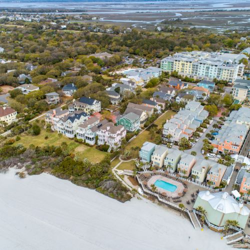 Aerial view of a coastal area with residential homes, beach, pools, and lush greenery stretching towards the horizon.