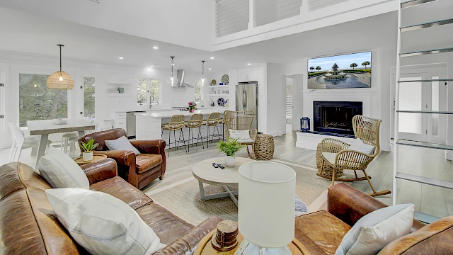A modern, open-concept living room and kitchen with leather seating, wicker chairs, and a fireplace under a wall-mounted TV.