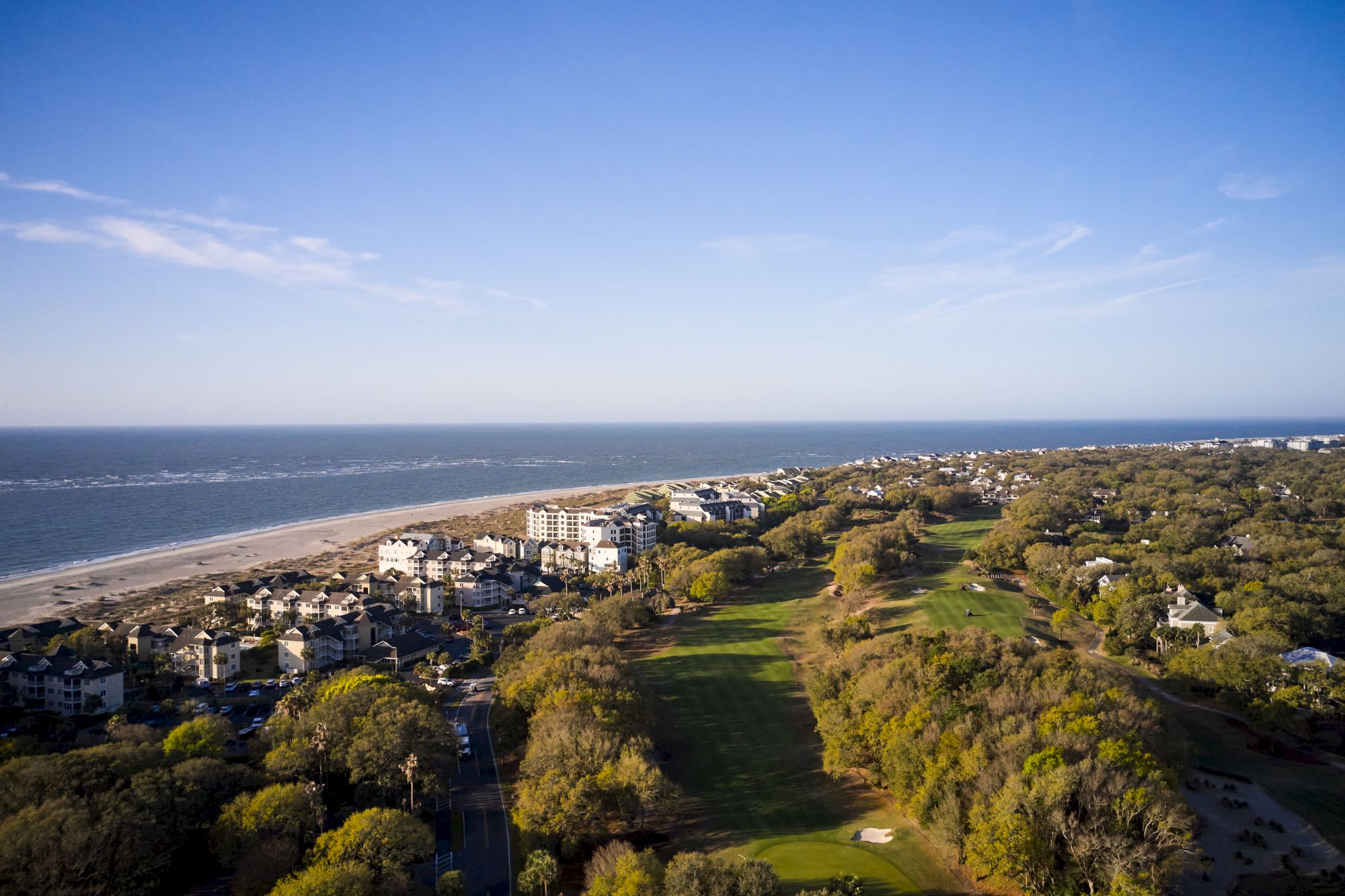 The image shows a coastal landscape with buildings, a beach, trees, and a grassy area near the shoreline.
