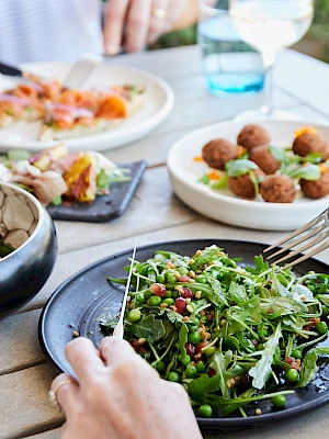 A table with a fresh salad, deviled eggs, croquettes, and other dishes, accompanied by two glasses of white wine on a sunny day.