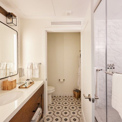 A modern bathroom features a sink, toilet, shower with glass door, towels, and a wooden vanity.