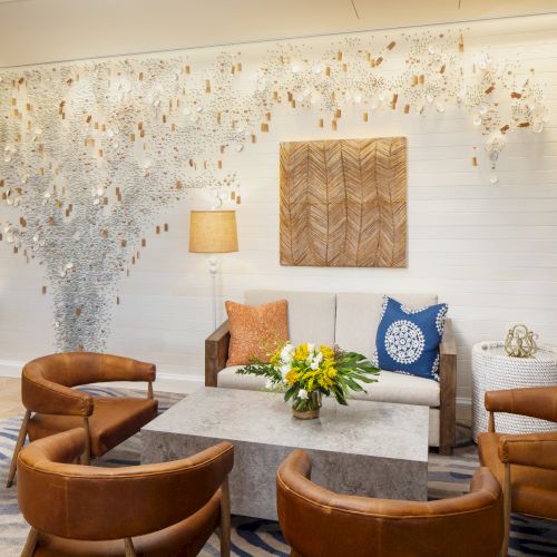 Modern hotel lobby with a white wall, brown leather chairs, a gray coffee table, yellow flowers, and an artful chandelier sculpture. end.