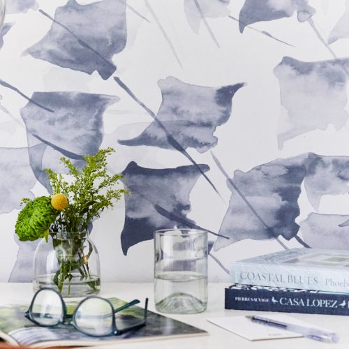 A desk with a floral vase, books, glasses, and a glass of water. There's a wallpaper with abstract leaf patterns in the background.