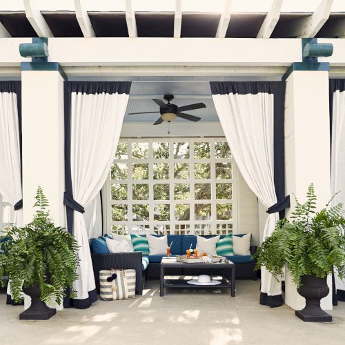 A stylish outdoor cabana with white curtains, comfy seating, vibrant cushions, plants, and drinks on a table, creating a relaxing atmosphere.