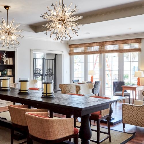 A stylish, modern living space with elegant lighting, a wooden table, plush chairs, a TV, and large windows offering natural light.