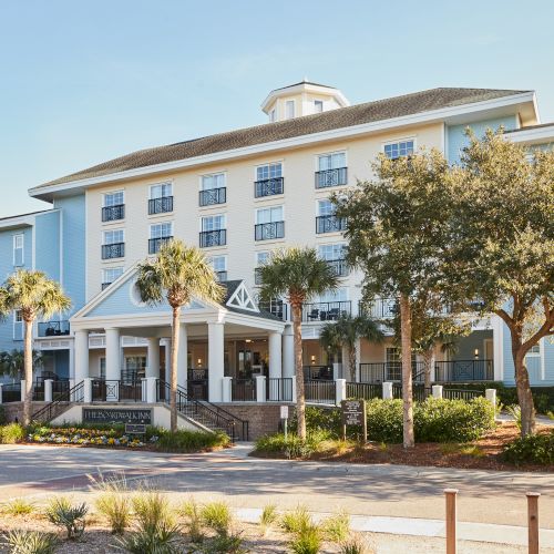 The image shows a large, multi-story hotel or inn with columns, palm trees, and landscaped grounds in front.