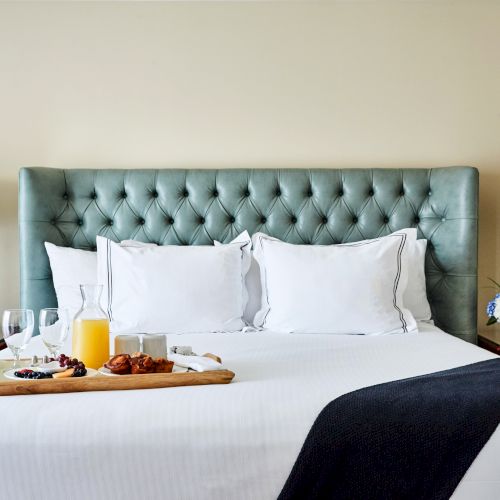 A neatly made bed with a tufted headboard, a tray of breakfast, two lamps, and a bouquet of blue and white flowers on side tables.
