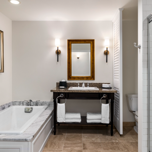 Modern bathroom with a bathtub, double sink vanity, mirror, toilet, shower, towels, and artwork on the wall.