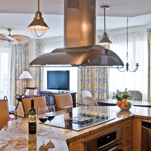 A modern kitchen with an island counter, wine glasses, a stove, and a cozy seating area near a TV and patterned curtains.