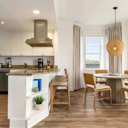 A modern kitchen and dining area, featuring a granite countertop, bar stools, woven chairs, a round table, and a pendant light.