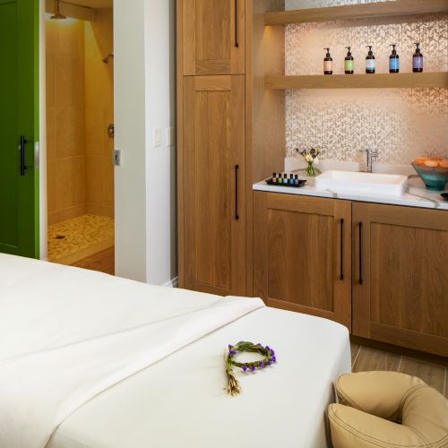 A spa room with a massage table, aromatherapy supplies, a sink, towels, and a shower area.