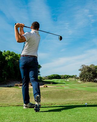A person is playing golf, swinging a club on a lush green course, under a clear blue sky.