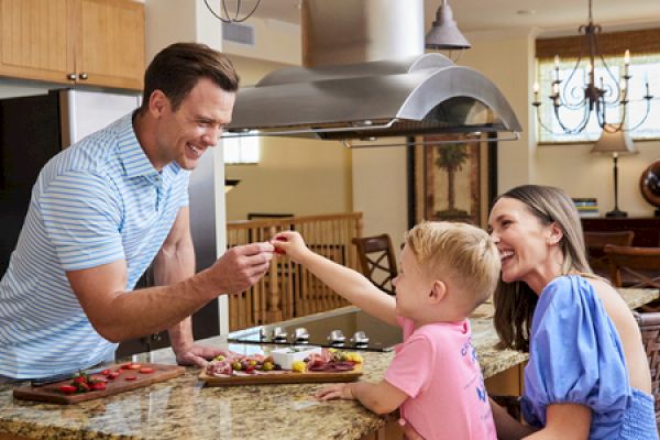 A family of three is in a kitchen, sharing a joyful moment around a counter with food, enjoying quality time together.