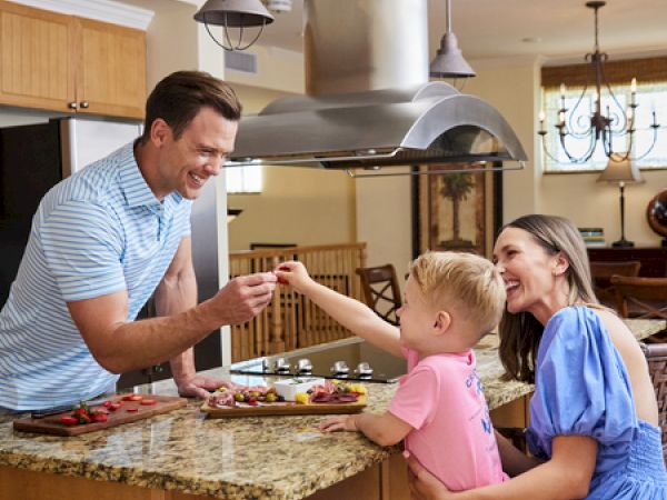 A family of three is in a kitchen, sharing a joyful moment around a counter with food, enjoying quality time together.