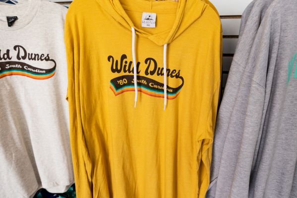 The image shows a clothing rack with various "Wild Dunes" branded shirts and hoodies in different colors, including a prominent yellow hoodie.