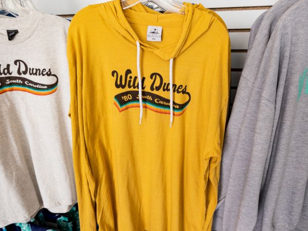 The image shows a clothing rack with various "Wild Dunes" branded shirts and hoodies in different colors, including a prominent yellow hoodie.