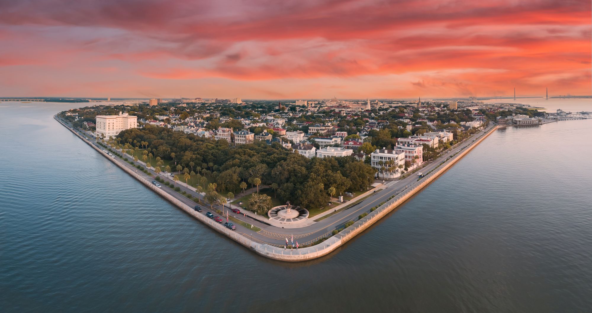 Aerial view of a triangular peninsula with urban landscape, surrounded by water, under a vibrant red-orange sky.