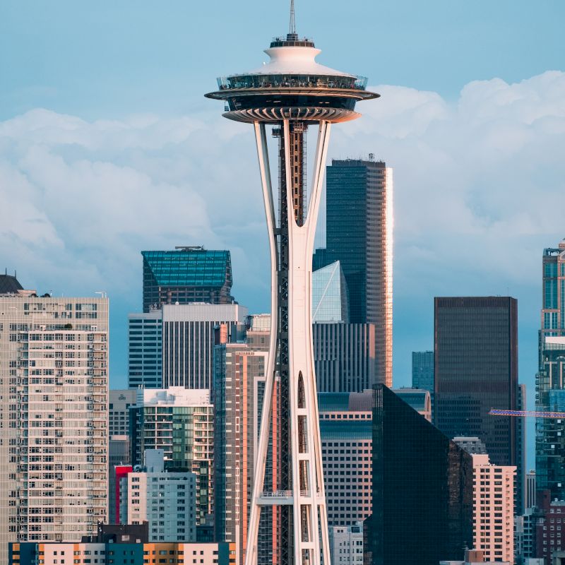 The image shows the Seattle skyline with the prominent Space Needle and surrounding skyscrapers under a blue sky with clouds.