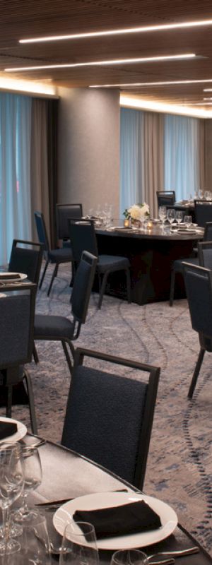 A banquet hall with round tables set elegantly for dining, featuring chairs, glassware, and centerpieces under warm lighting.