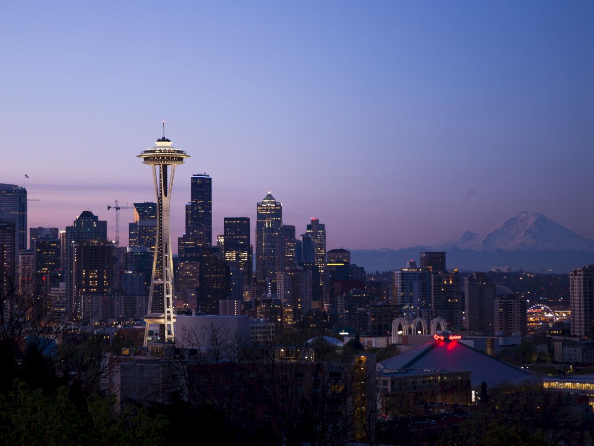 Seattle skyline at dusk with the Space Needle and Mount Rainier in the background, under a purple sky.