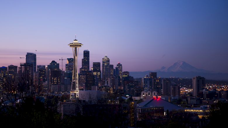 Seattle skyline at dusk with the Space Needle and Mount Rainier in the background, under a purple sky.